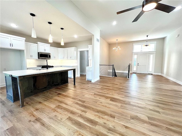 kitchen featuring tasteful backsplash, decorative light fixtures, light hardwood / wood-style floors, a center island with sink, and white cabinetry