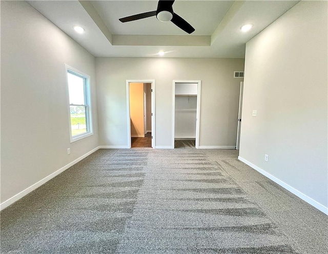 unfurnished bedroom featuring a spacious closet, ceiling fan, a closet, and a raised ceiling