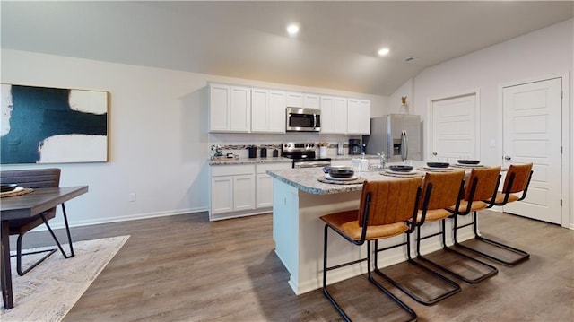 kitchen with a kitchen island with sink, white cabinets, a kitchen breakfast bar, vaulted ceiling, and stainless steel appliances