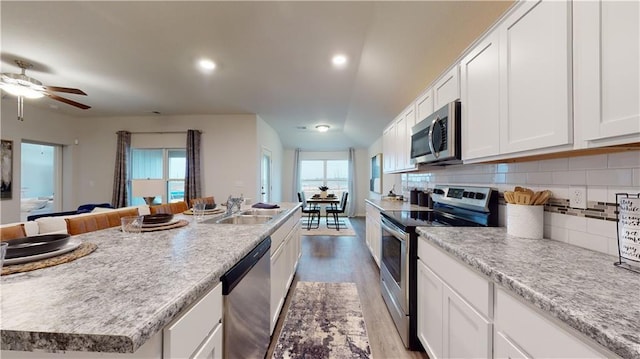 kitchen with stainless steel appliances, sink, a center island with sink, light hardwood / wood-style floors, and white cabinetry