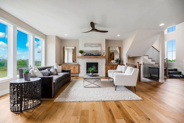 living room with a fireplace, plenty of natural light, ceiling fan, and light wood-type flooring