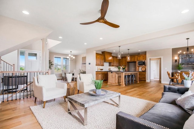 living room featuring ceiling fan with notable chandelier and light wood-type flooring