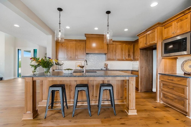 kitchen featuring built in microwave, custom exhaust hood, an island with sink, and a breakfast bar area