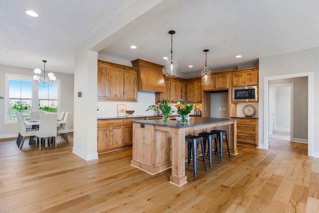 kitchen with built in microwave, a breakfast bar area, custom exhaust hood, light wood-type flooring, and a kitchen island