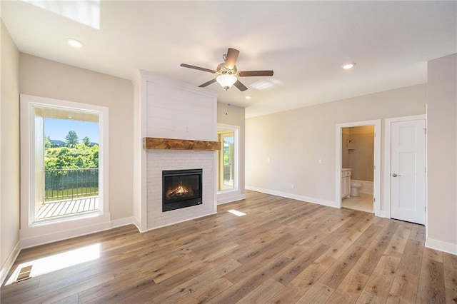 unfurnished living room with hardwood / wood-style flooring, ceiling fan, and a large fireplace