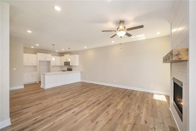 unfurnished living room featuring light hardwood / wood-style flooring, ceiling fan, and a brick fireplace