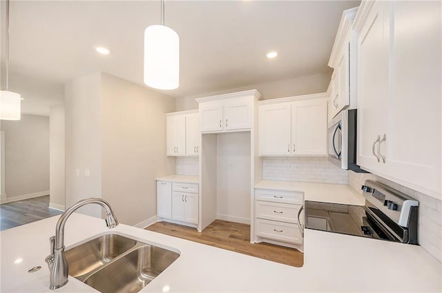 kitchen with appliances with stainless steel finishes, sink, white cabinets, and hanging light fixtures