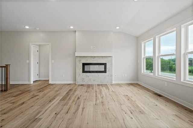 unfurnished living room featuring light wood-type flooring, vaulted ceiling, and a high end fireplace