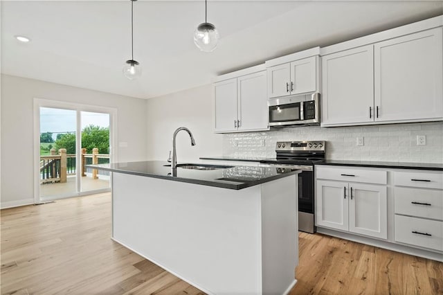 kitchen with appliances with stainless steel finishes, hanging light fixtures, light hardwood / wood-style floors, an island with sink, and sink