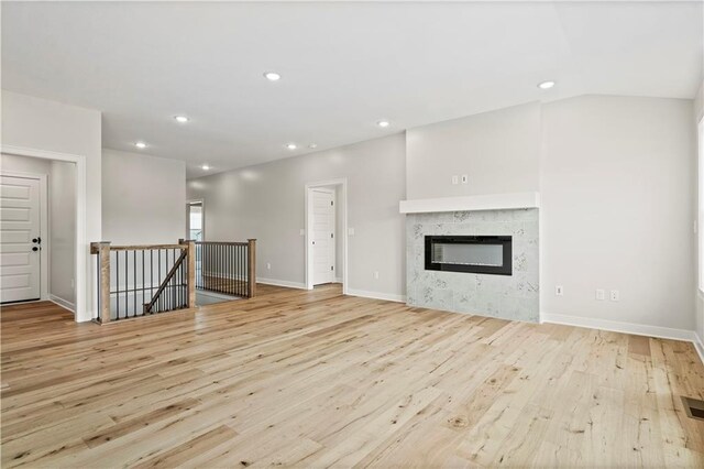 unfurnished living room featuring light hardwood / wood-style flooring, a high end fireplace, and lofted ceiling