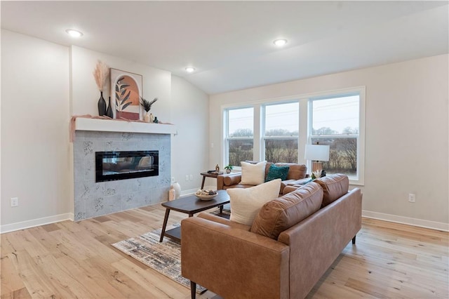 living room featuring lofted ceiling, light hardwood / wood-style flooring, and a tile fireplace