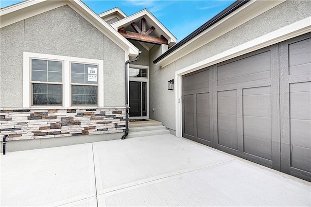 view of exterior entry featuring a garage, stone siding, and stucco siding