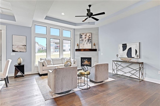 living room featuring a raised ceiling, a tile fireplace, ceiling fan, and wood-type flooring