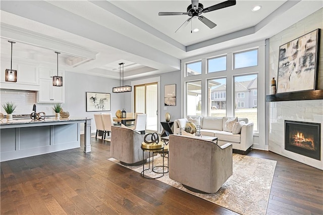 living room with a tray ceiling, a tile fireplace, ceiling fan, and dark hardwood / wood-style floors