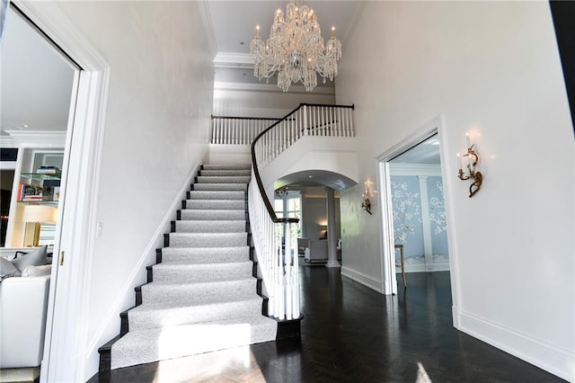 stairway with a high ceiling, ornamental molding, and a notable chandelier