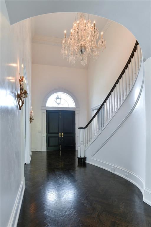 entryway with ornamental molding, a towering ceiling, dark parquet floors, and a chandelier