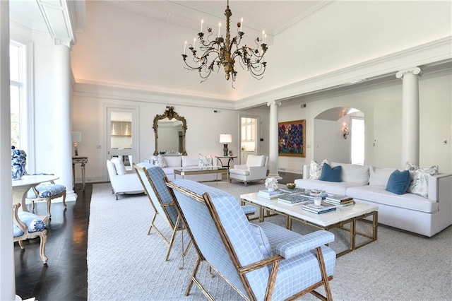 living room featuring a wealth of natural light, a notable chandelier, a towering ceiling, and ornate columns