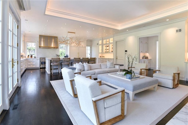 living room featuring dark wood-type flooring, a wealth of natural light, a raised ceiling, and ornamental molding