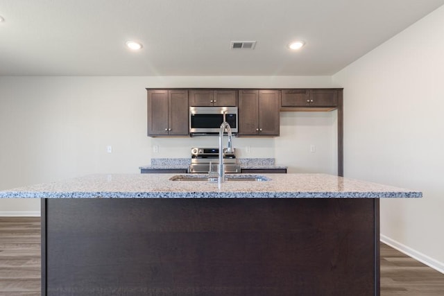 kitchen with dark hardwood / wood-style flooring, light stone countertops, sink, and a center island with sink