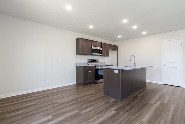 kitchen featuring an island with sink, dark brown cabinetry, electric range oven, dark hardwood / wood-style floors, and sink