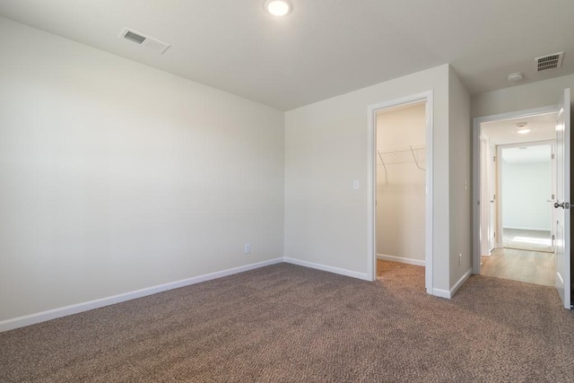 unfurnished bedroom with a walk in closet, light colored carpet, and a closet