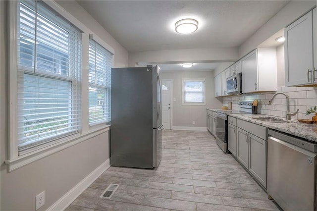 kitchen featuring light hardwood / wood-style floors, light stone countertops, appliances with stainless steel finishes, backsplash, and sink