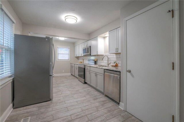 kitchen with light stone counters, white cabinets, stainless steel appliances, backsplash, and sink