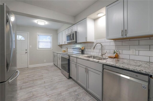 kitchen with sink, light stone counters, appliances with stainless steel finishes, light hardwood / wood-style floors, and tasteful backsplash