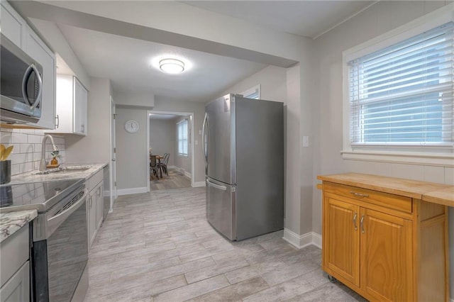 kitchen with sink, appliances with stainless steel finishes, tasteful backsplash, white cabinetry, and light wood-type flooring