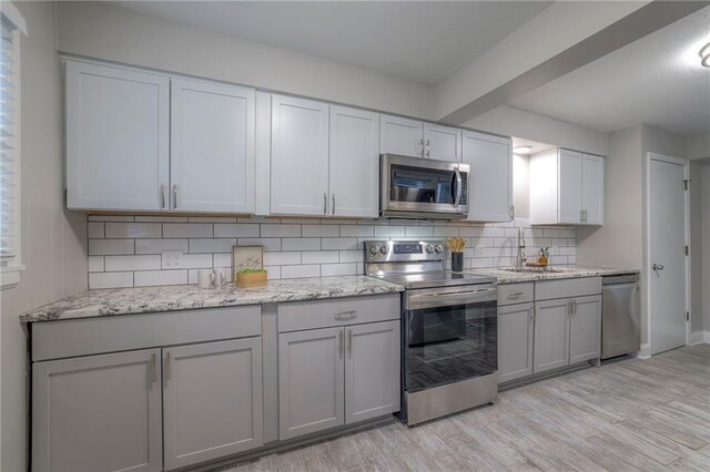 kitchen with appliances with stainless steel finishes, gray cabinetry, light wood-type flooring, and tasteful backsplash