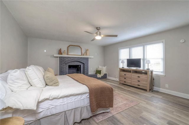 bedroom with a brick fireplace, light hardwood / wood-style floors, and ceiling fan