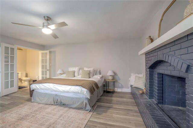 bedroom featuring connected bathroom, hardwood / wood-style floors, ceiling fan, and a brick fireplace