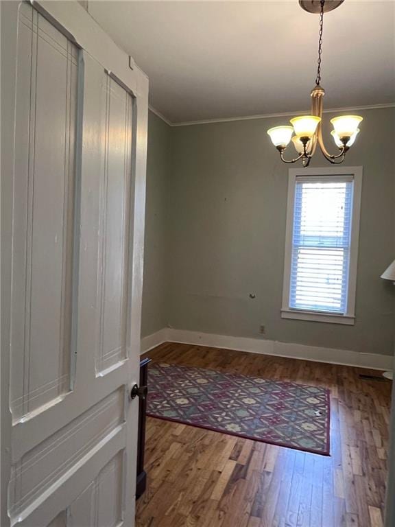 empty room featuring an inviting chandelier, ornamental molding, and hardwood / wood-style flooring