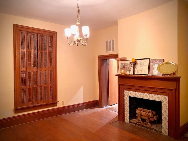 unfurnished living room featuring a tile fireplace, dark wood-type flooring, and a chandelier