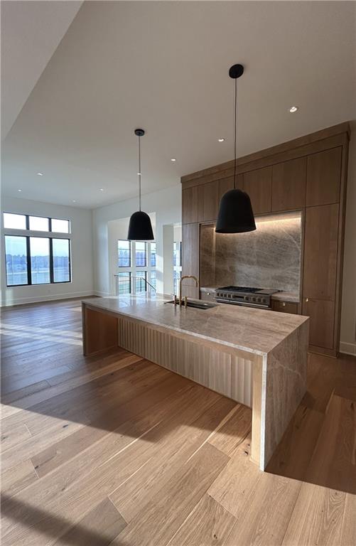 kitchen featuring sink, hanging light fixtures, high end stove, an island with sink, and light hardwood / wood-style floors