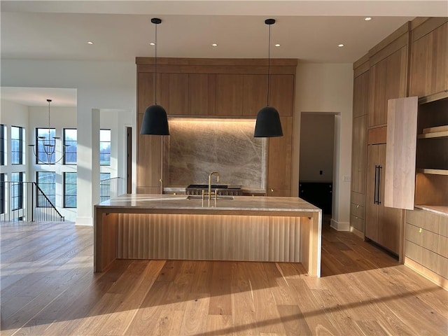 kitchen with backsplash, light hardwood / wood-style floors, hanging light fixtures, and a center island with sink