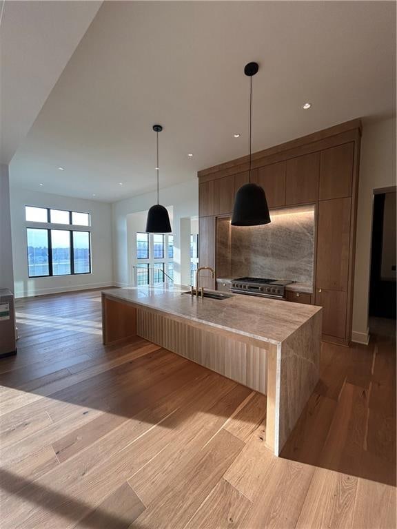 kitchen with sink, hanging light fixtures, decorative backsplash, a center island with sink, and light wood-type flooring