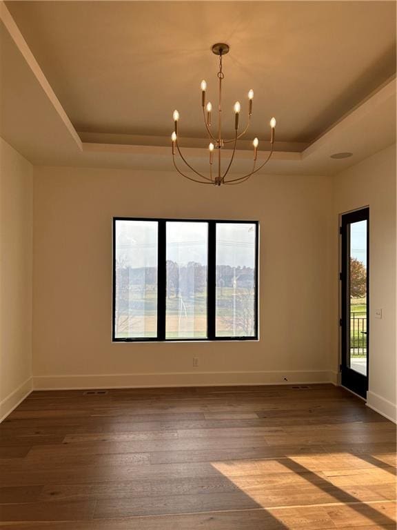 unfurnished room with a chandelier, wood-type flooring, a wealth of natural light, and a tray ceiling