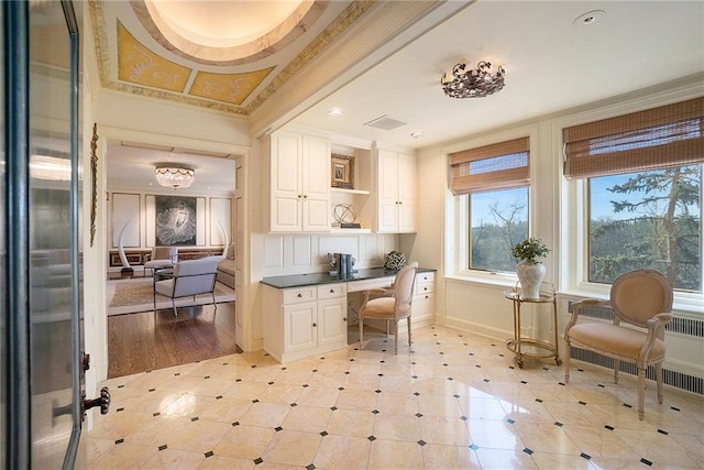 office space featuring ornamental molding, built in desk, and light hardwood / wood-style floors