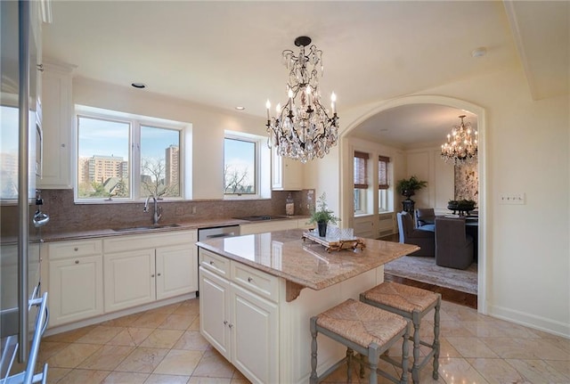 kitchen with hanging light fixtures, sink, tasteful backsplash, white cabinetry, and a center island