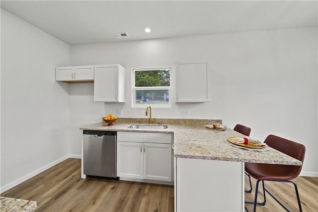 kitchen with light wood-type flooring, white cabinets, a breakfast bar, sink, and dishwasher