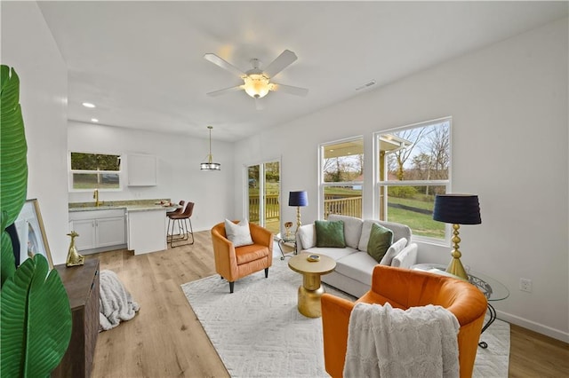 living room featuring light hardwood / wood-style floors, ceiling fan, and a healthy amount of sunlight