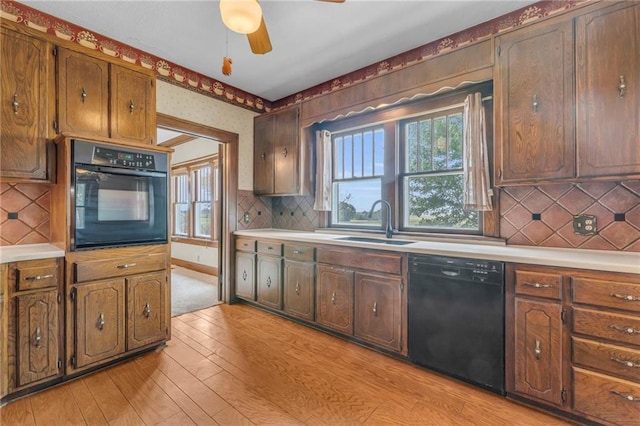 kitchen featuring light wood-type flooring, sink, black appliances, ceiling fan, and tasteful backsplash