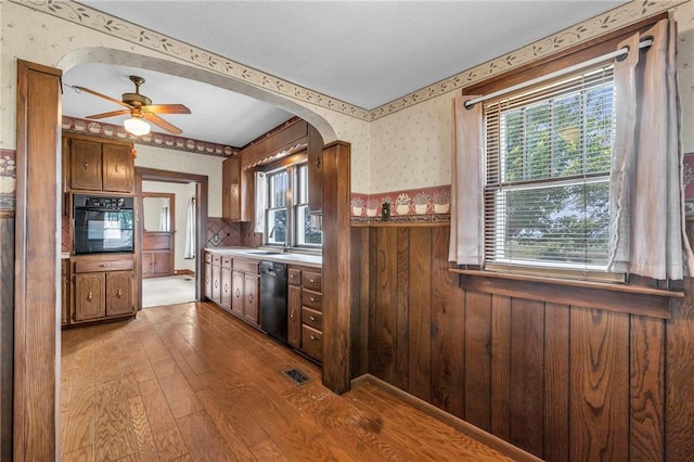 kitchen featuring hardwood / wood-style flooring, sink, black appliances, wood walls, and ceiling fan