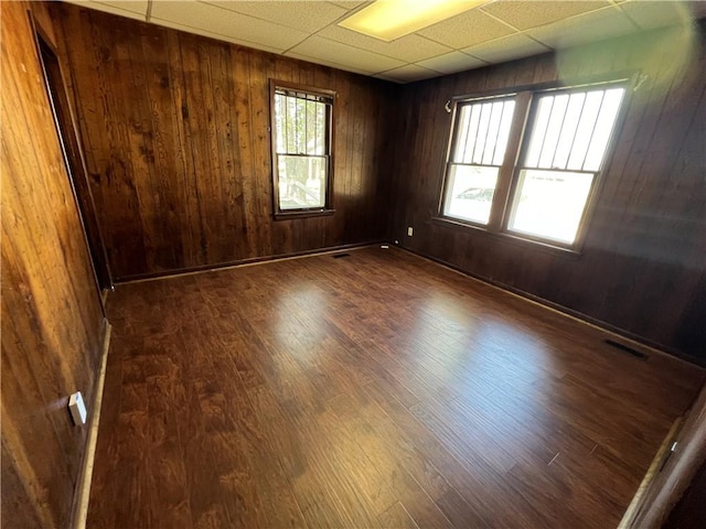 empty room with dark wood-type flooring, wooden walls, and a drop ceiling