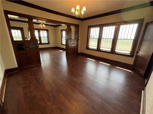 empty room featuring dark wood-type flooring, decorative columns, a chandelier, and crown molding