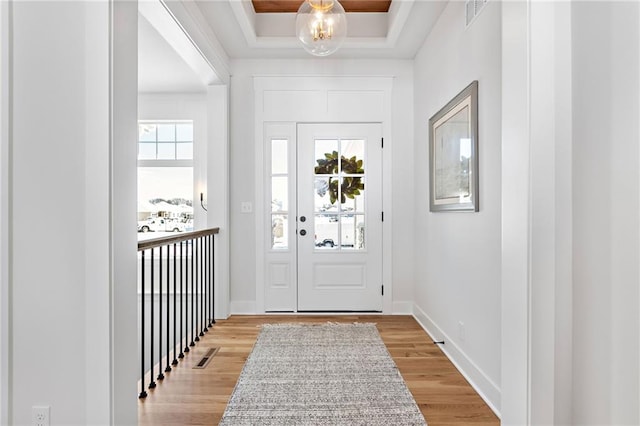 foyer entrance with hardwood / wood-style flooring, a tray ceiling, and a notable chandelier