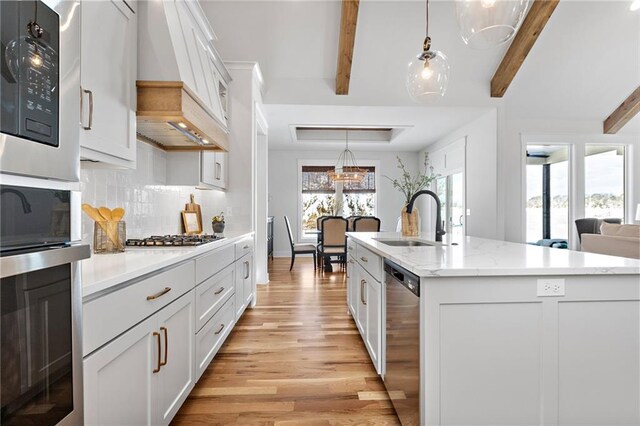 20287 Barker St, Spring Hill, KS 66083 - kitchen featuring light wood finished floors, premium range hood, appliances with stainless steel finishes, decorative backsplash, and a center island with sink