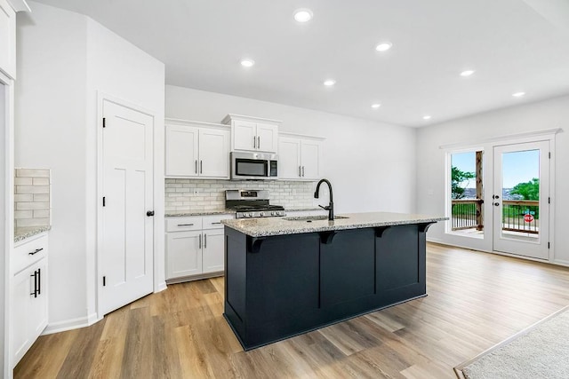 kitchen with sink, stainless steel appliances, light hardwood / wood-style flooring, and light stone countertops