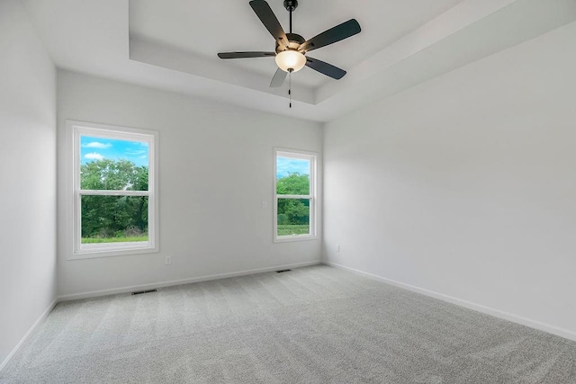 carpeted empty room featuring ceiling fan and a raised ceiling